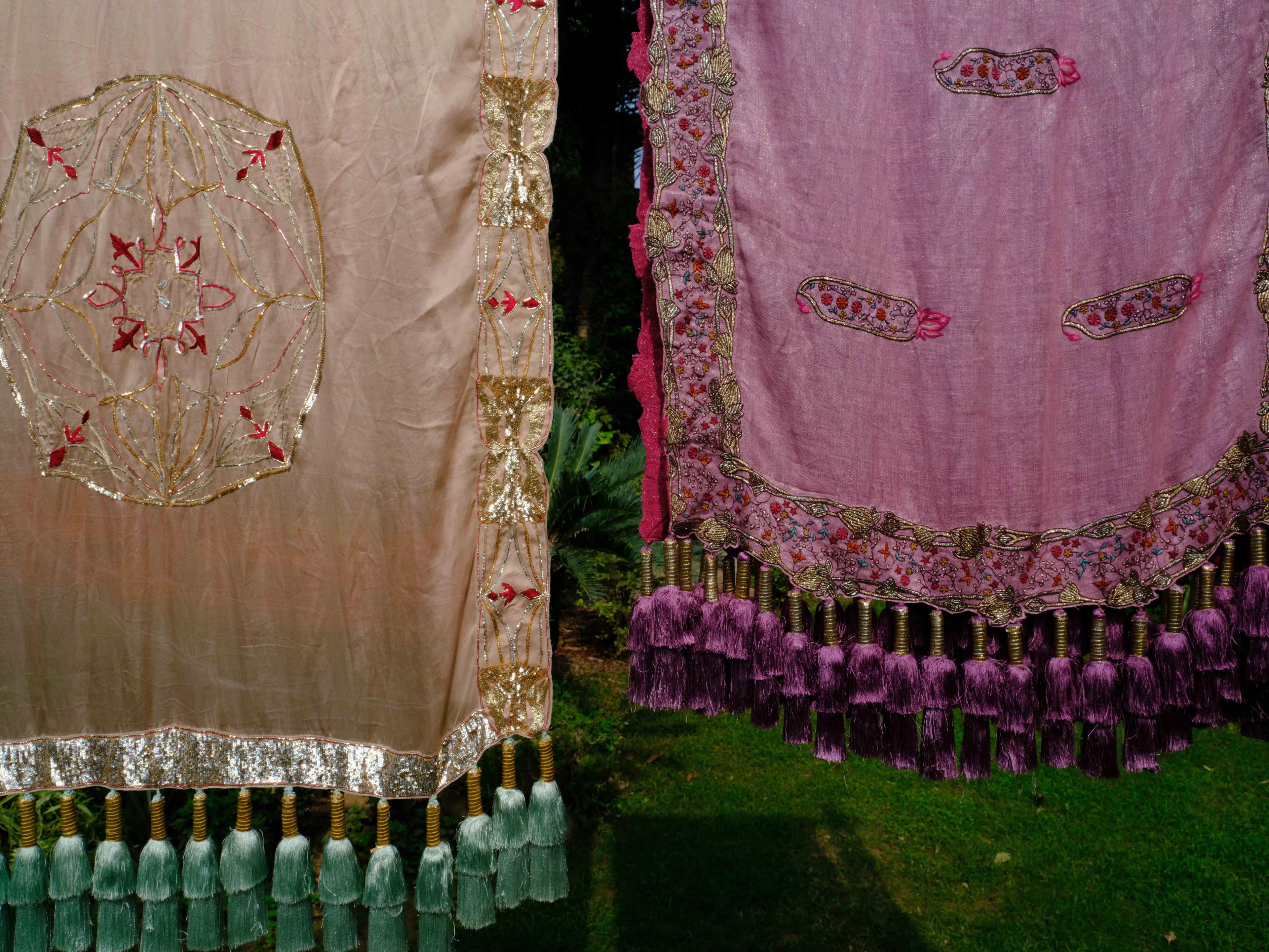 Two embroidered chunnis with tasselled borders, hung in a garden